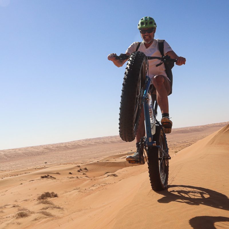 un vététiste en fat bike dans le désert, sur la roue arrière
